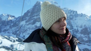 Kışlık giysiler giyen, dağ zirvesinin tepesinden İsviçre Alpleri manzarasının keyfini çıkaran bir kadın manzaraya bakıyor.