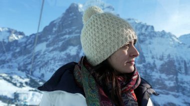 Kışlık giysiler giyen, dağ zirvesinin tepesinden İsviçre Alpleri manzarasının keyfini çıkaran bir kadın manzaraya bakıyor.