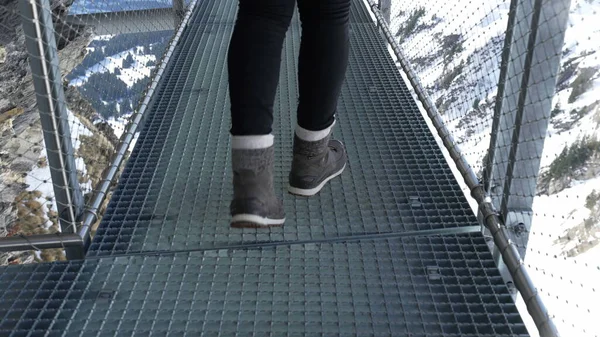 Person carefully walking through metal handrail support by cliffside in Swiss alps adventure, closeup view of prudent woman scared by elevated mountain view
