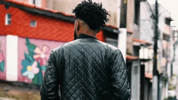 若いアフリカ系アメリカ人男性が街の通りを歩き 黒と白のジャケットを手にした 都市環境で外を歩く20代の思慮深いペンシルベニア — ストック動画