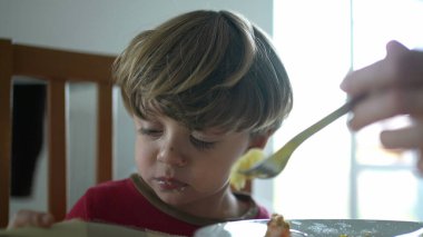 Çocuk öğle yemeği saatinde yemeği reddediyor, ebeveyn küçük çocuğu beslemeye çalışıyor, çocuk yemek saatinde üzülüyor.