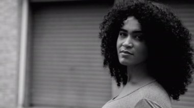 Urban Setting 'de güçlendirilmiş Afro-Amerikan Kadını, Cesur siyah beyaz, tek renkli Genç Kadın Yüzünün Yakın Çekimini İzliyor. Sokakta dikilip kameraya bakan bir zenci.