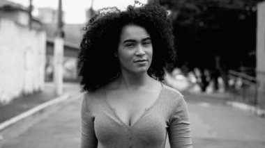 Kendine güvenen genç siyah bir kadın şehir sokaklarında tek renkli, siyah ve beyaz yoğun bir şekilde kameraya doğru yürüyor. Kıvırcık saçlı Afrikalı Amerikalı 20 'li yaşlardaki kız.