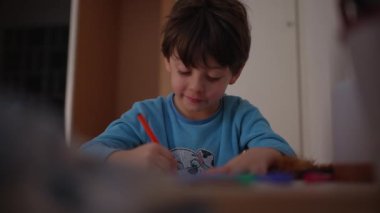 Yatmadan önce pijama giymiş, evde çizim yapan mutlu bir çocuk. Kağıt üzerinde gülümseyen yaratıcı renklerle meşgul bir çocuk