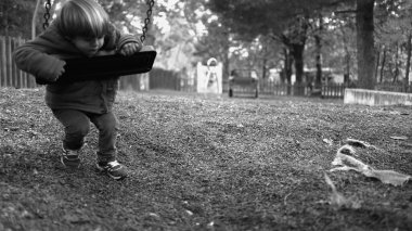 Park salıncağına yaslanan yalnız küçük bir çocuk dışarıda salıncak sallıyor tek renkli ve beyaz bir parkın ortasında yalnızlık çekiyor. Çocukluk depresyonu kavramı