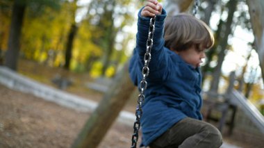 Sonbahar sezonunda parkta sallanan küçük bir çocuk. 3 yaşındaki çocuk dışarıda oynuyor.