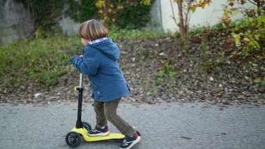 Kapalı çocuk ayakları dışarıda üç tekerlekli scooter sürüyor.