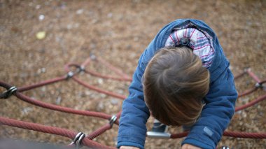 Sonbahar sezonunda çocuk parkının iplerine tırmanırken mutlu ol. 3 yaşındaki bir çocuğun dışarıda eğlendiği bir sonbahar günü oyunu. Mavi ceket giyiyor ve fiziksel çaba gösteriyor.