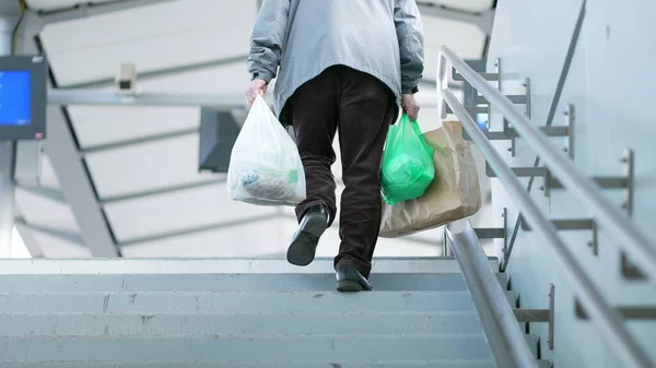 Person carries grocery bags during daily commute walking up the stairs heading toward train platform