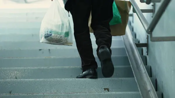 Person Carrying Groceries Up Stairs from Underground Train. Daily Commuter with Groceries Ascending Stairs from Subway