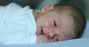Cute happy newborn baby smiling feedling joy, infant first week of life in bed