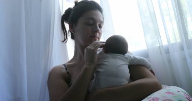 Mom holding newborn baby next to window curtain