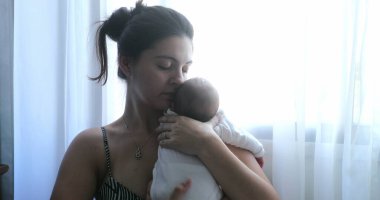 Mom holding newborn baby son in her arms, real life and candid family moment