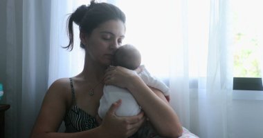 Mom holding newborn baby son in her arms, real life and candid family moment