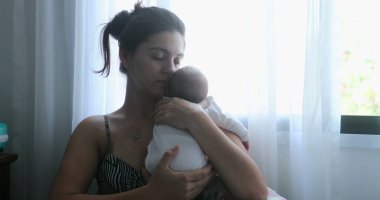 Mom holding newborn baby son in her arms, real life and candid family moment