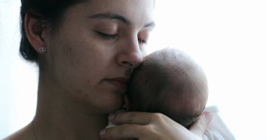 Mom holding newborn baby son in her arms, real life and candid family moment