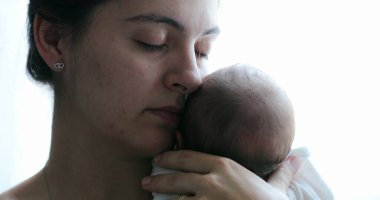 Mom holding newborn baby son in her arms, real life and candid family moment