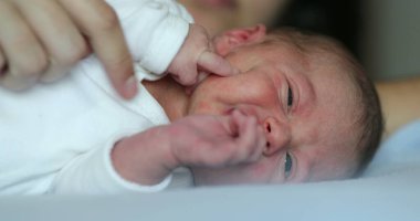 Newborn baby infant crying laying in bed, close-up of baby face crying