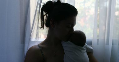 Silhouette of mother holding newborn baby son in her arms next to window