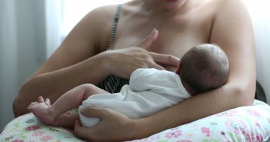Mother breastfeeding newborn baby next to window
