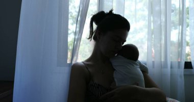 Silhouette of mother holding newborn baby son in her arms next to window