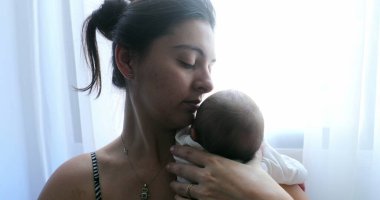 Mother holding newborn baby next to home window, first week of life