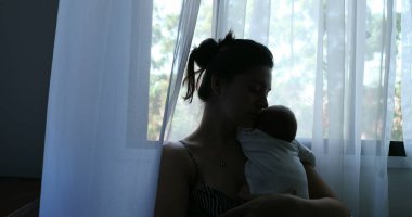 Silhouette of mother holding newborn baby son in her arms next to window
