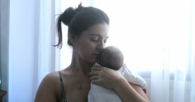 Newborn baby being held by mother in first week of life, mom holding baby son by window
