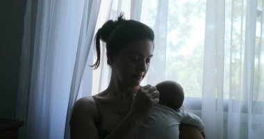 Mother holding newborn baby next to window