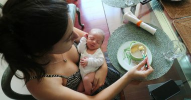 Mother holding newborn baby while eating dessert food meal