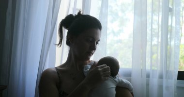 Mother holding newborn baby next to window