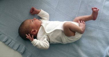 Newborn baby infant during first week of life, baby laid in bed seen from above