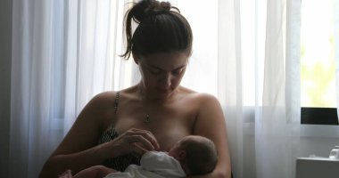 Mother breastfeeding newborn baby next to window