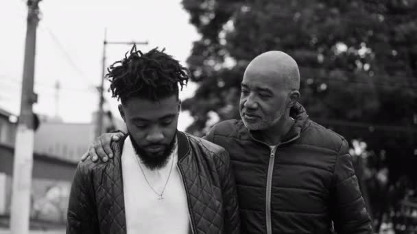 父亲和儿子的谈话 中年非洲裔美国父亲辅导成年儿子手牵着手 应该在城市街道上单色 黑白漫步 — 图库视频影像