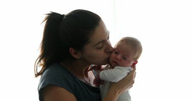 Mother kissing her newborn baby son during first days of life