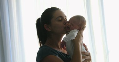 Mother showing love and affection kissing newborn baby infant next to curtain window