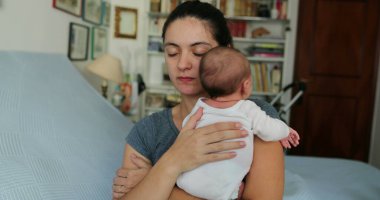 Mom tapping newborn baby in the back helping with hiccups