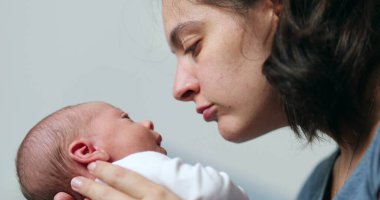 Mother and newborn baby interaction mom kissing infant during first day of life showing love and affection