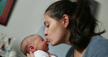 Mother and newborn baby interaction mom kissing infant during first day of life showing love and affection