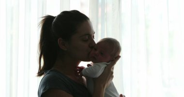 Mother kissing newborn baby infant next to window curtain