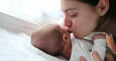 Mother kissing newborn baby infant showing love affection and baby care