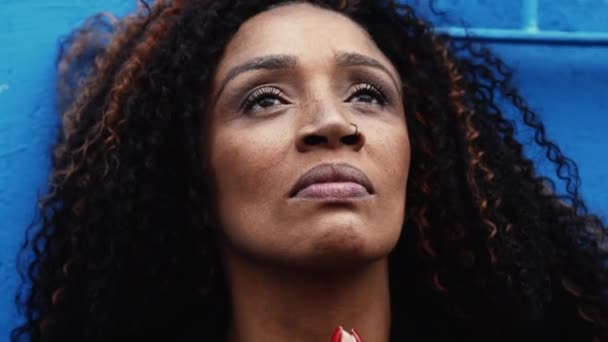 忠实的黑人南美女人凝视着天空 站在城市的背景下 靠着蓝色的墙壁 非洲裔宗教妇女抬起头来感受到上帝的存在 — 图库视频影像