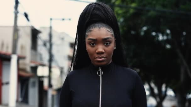 一位20多岁的年轻的南美黑人女孩站在街上看着摄像机 追踪一位在城市环境中严肃而中立的人的近照 — 图库视频影像