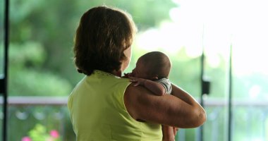 Back of grand-mother holding newborn baby infant in arms candid