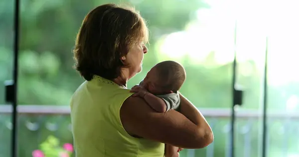 Back of grand-mother holding newborn baby infant in arms candid