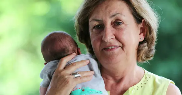 Portrait of grand mother holding newborn baby grand-son looking to camera