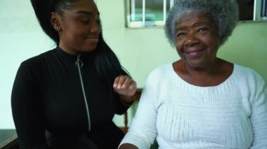 Afrikalı Amerikalı torun büyükannenin elini tutuyor ve aile üyelerine sevgisini ve desteğini gösteriyor. Genç kız büyükannesinin alnından öpüyor.
