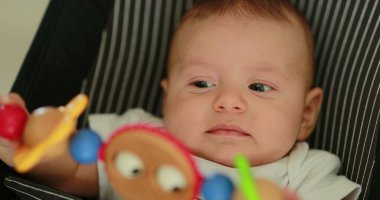 Baby newborn in chair seated with spinning toy in the foreground