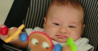 Baby newborn in chair seated with spinning toy in the foreground