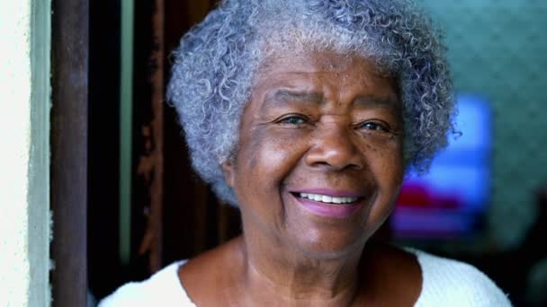 アフリカ系アメリカ人の80代の幸せな黒人高齢女性がカメラで笑っている 住宅に立っているしわと喜びの表現を持つ灰色の椅子の女性の肖像 — ストック動画